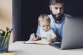 Man and little baby sitting in front of laptop. Serious and busy father with small child on his knees trying to work remotely Royalty Free Stock Photo