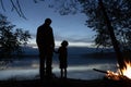 A man and a little boy father and son hold hands, stand on the shore and talk against the background of a bonfire and the reflecti Royalty Free Stock Photo