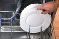 A man loads dirty dishes, plates, spoons, forks, cutlery into dishwasher tray Royalty Free Stock Photo