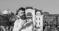 Man with long beard enjoy coffee. Man with beard and mustache on calm face drinks coffee at balcony, urban background