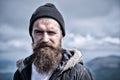 Man with long beard and mustache wears hat. Hipster on strict face with beard looks brutally while hiking. Masculinity Royalty Free Stock Photo