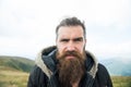 Man with long beard and mustache wears jacket. Hipster on strict face with beard looks brutally while hiking. Hermit