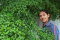 A man with a Long hair and a mustache peeking out from the bushes of Terminalia ivorensis Chev