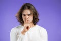 Man with long hairstyle holding finger on lips over violet background. Gesture of shhh, secret, silence. . High quality Royalty Free Stock Photo