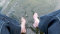 Man in long shorts dangles his legs in the water of lake. splashing water. slow motion