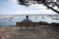 Man looking at boats and ships sailing on seascape while sitting on bench