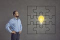 Man looking at a complete jigsaw puzzle with a bright idea light bulb in the centre