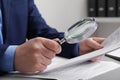 Man looking at document through magnifier at white table, closeup. Searching concept