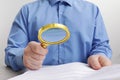 Man looking at document through magnifier at white wooden table, closeup. Searching concept