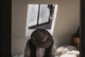 A man looking down wearing a fedora hat and waistcoat sitting on a bed with a window behind. With a classic edit
