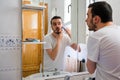 Man looking at himself in a mirror in the bathroom. He is shaving his beard Royalty Free Stock Photo