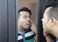 A man looking at his reflection in mirror nose picking and checking his nasal cavity for nose infection and nasal bleed