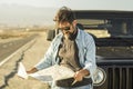 Man looking at map leaning on vehicle at roadside. Mature man checking location of destination on paper map standing outside car.