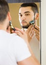 Man looking at mirror and shaving face with razor Royalty Free Stock Photo