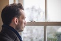 A Caucasian man looking out window, feeling sad, seasonal affective disorder