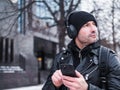 Man looking for a place using GPS map in smartphone. He lost in unknown city. he is dressed in a leather jacket, hat and Royalty Free Stock Photo