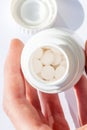 Man looking into a small open pill container with white pills inside in a sterile environment, holding it in his hand, examining