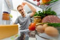 Man looking for something to eat at night while standing in front of opened fridge. Unhealthy eating concept. Picture taken from Royalty Free Stock Photo