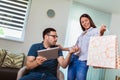 Man looking troubled when shopaholic woman arriving home with shopping bags