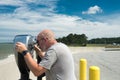 Man looks through Coin binoculars at ocean