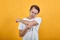 Man looks at her elbow, bruised pain. Guy in white t-shirt on yellow background Royalty Free Stock Photo