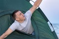 Man looks out of the tent and stretching. Morning in nature