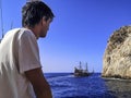 A man looks at a pirate ship in the Mediterranean Sea near a rock in Alanya Turkey. A tourist in a white T-shirt admires the