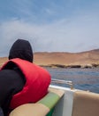 Man lost in thought admires the view, is wearing a life jacket inside a boat, sand dune on the background, and the sea Royalty Free Stock Photo