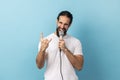 Man loudly singing song holding microphone in hand, having fun resting in karaoke, showing rock sign Royalty Free Stock Photo