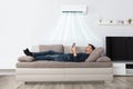 Man Lying On Couch Under Air Conditioner Using Tablet