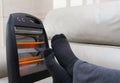 Man lying on sofa with electric heater near his feet Royalty Free Stock Photo