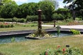 A man made pond with water plants and a sculpture surrounded by pathways and a rose garden in Boerner Botanical Gardens