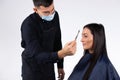 A man make-up artist in a medical mask makes a lady`s makeup on a white background. Studio shot on white background