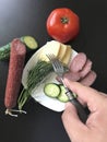 The man makes an easy snack. On the saucer are sausage, cucumber, tomato, cheese and dill.