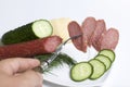 The man makes an easy snack. On the saucer are sausage, cucumber, tomato, cheese and dill.