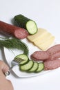 The man makes an easy snack. On the saucer are sausage, cucumber, tomato, cheese and dill.