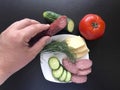 The man makes an easy snack. On the saucer are sausage, cucumber, tomato, cheese and dill.