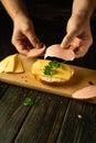 A man makes a sandwich on a cutting board. Sausage and cheese on bread. Fast food concept on the kitchen table at home. Place for Royalty Free Stock Photo