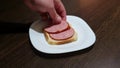 A man makes a sausage and cheese sandwich on a white plate