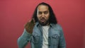Man making a beckoning hand gesture and scowling face in studio with pink wall and denim jacket; anger confrontation Royalty Free Stock Photo