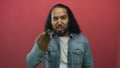Man making a beckoning hand gesture and scowling face in studio with pink wall and denim jacket; anger confrontation Royalty Free Stock Photo