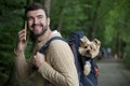 Man making a call while hiking in the forest with his dog inside a backpack