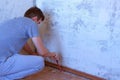 Man making renovation, removing plinth from old wall and floor using crowbar.