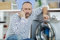 Man making telephone call crouched beside washing machine Royalty Free Stock Photo