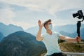 Man making video on camera for travel blogg, wearing protective mask at mountains view Royalty Free Stock Photo