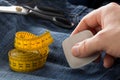 Man marking line with tailor`s chalk on jeans denim fabric with scissors and measuring tape on blue jeans denim close up - jeans