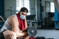 Man with mask doing biceps exercises with dumbbells in the gym. sitting on a bench. Covid19, coronavirus. Health and wellness Royalty Free Stock Photo