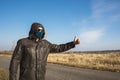 A man in a mask and goggles in the countryside tries to stop a passing car or taxi, a concept of movement under coronavirus