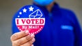 Man in mask from minority group produly holds Voted By Mail sticker during US Election closeup