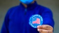 Man in mask from minority group produly holds Voted By Mail sticker during US Election closeup